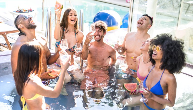 Side view of happy friends group drinking white wine champagne at swimming pool party – Luxury vacation concept with young guys and girls having fun in summer day at hotel resort – Warm bright filter